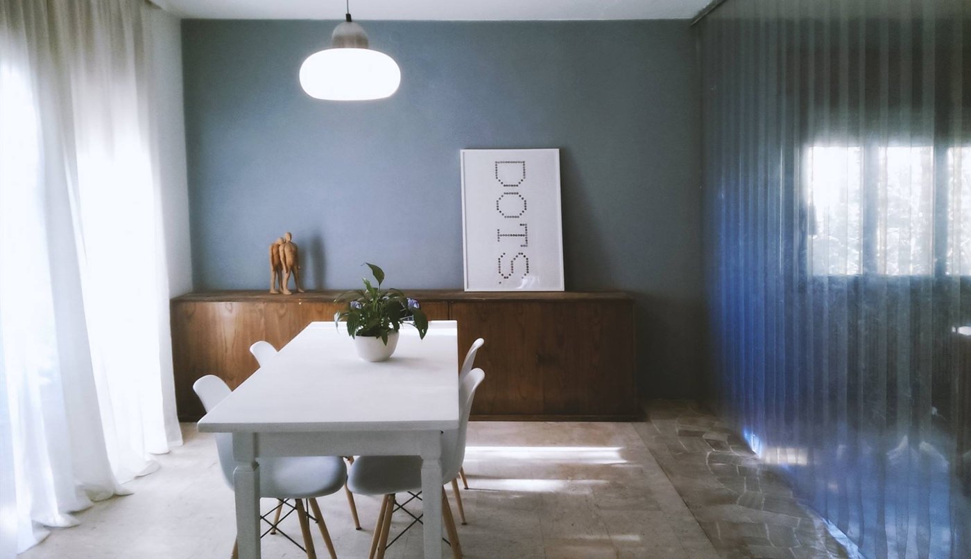 A lived-in dining room with blue-grey walls, warm wood, white furniture and soft daylight